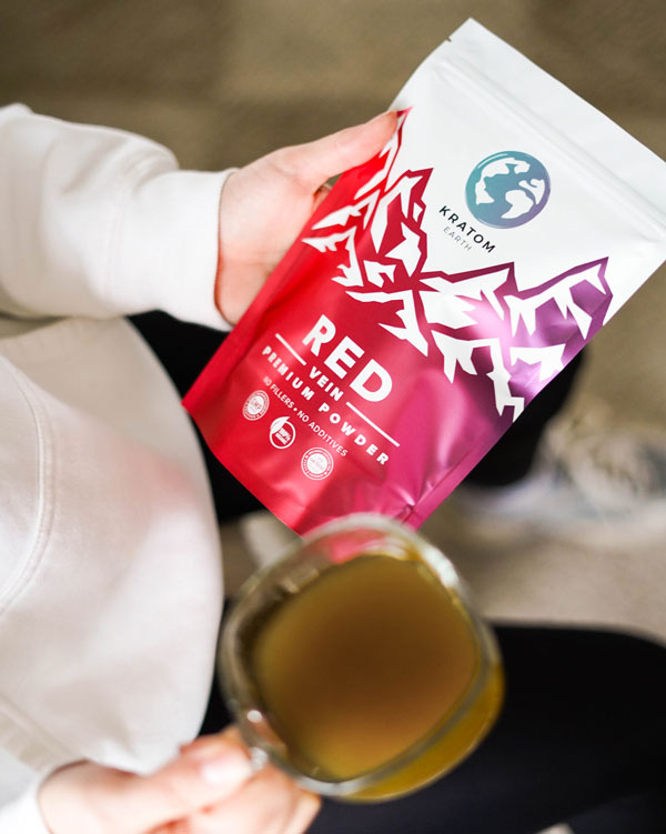 A person holds a pouch labeled "Red Vein Powder" and a cup of greenish-brown beverage, showcasing their recent Kratom Online purchase.